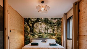 Une chambre à coucher avec un lit, des murs en bois, une fresque représentant une forêt et une fenêtre.