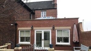 A brick house with a gated entrance, two windows with white frames, and a small porch area. - The Old Rectory  (Jarrow)