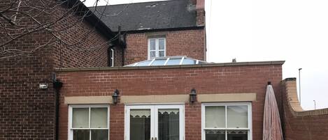 A brick house with a gated entrance, two windows with white frames, and a small porch area.