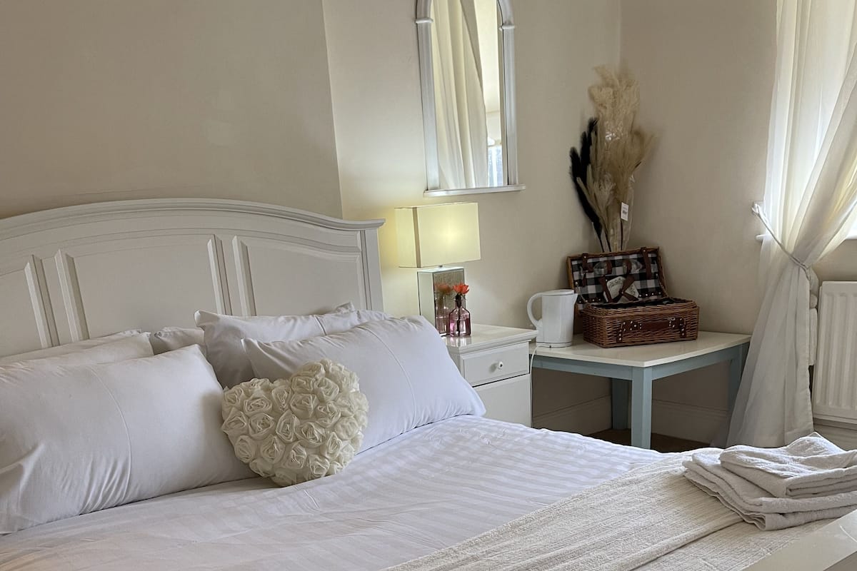 A neatly made bed with white linens, a bedside table with a lamp, and a mirror on the wall.