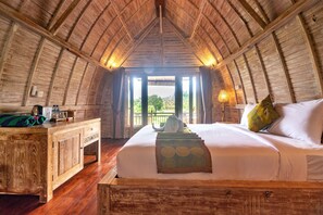 A cozy, wooden-paneled room with a bed, bedside table, and a view through a large window. - AlamGangga Villas Tirta Gangga (Karangasem)