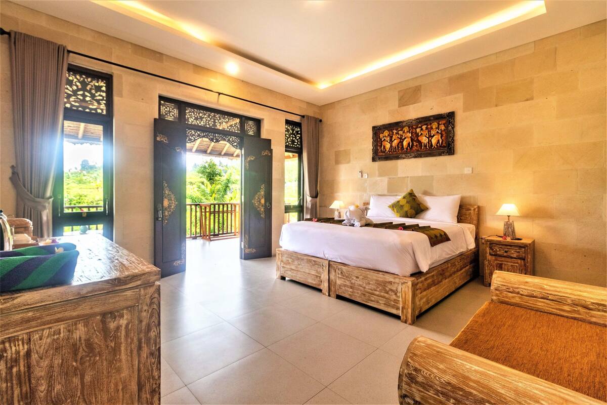 A bedroom with a wooden bed, a nightstand, and a view of a garden through a door.