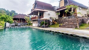 A poolside area with lounge chairs and a stone wall. - AlamGangga Villas Tirta Gangga (Karangasem)