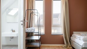 Une chambre avec un lit superposé, une petite table avec des serviettes, une fenêtre avec des rideaux et un lavabo blanc.