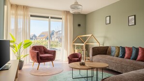 Un salon comprenant un canapé, deux fauteuils, une table basse, un téléviseur et une plante.