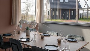 Une table à manger dressée pour six personnes, avec des chaises, un vase rempli d’orchidées blanches et une vue sur un bâtiment par la fenêtre.