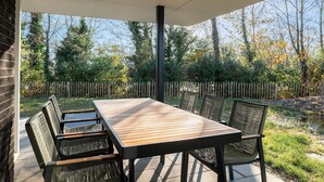 Une terrasse couverte avec une table et des chaises en bois, entourée d’une clôture en bois et d’arbres.