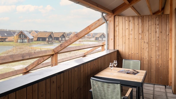 Een houten balkon met een tafel en stoelen, met uitzicht op een rij huizen.
