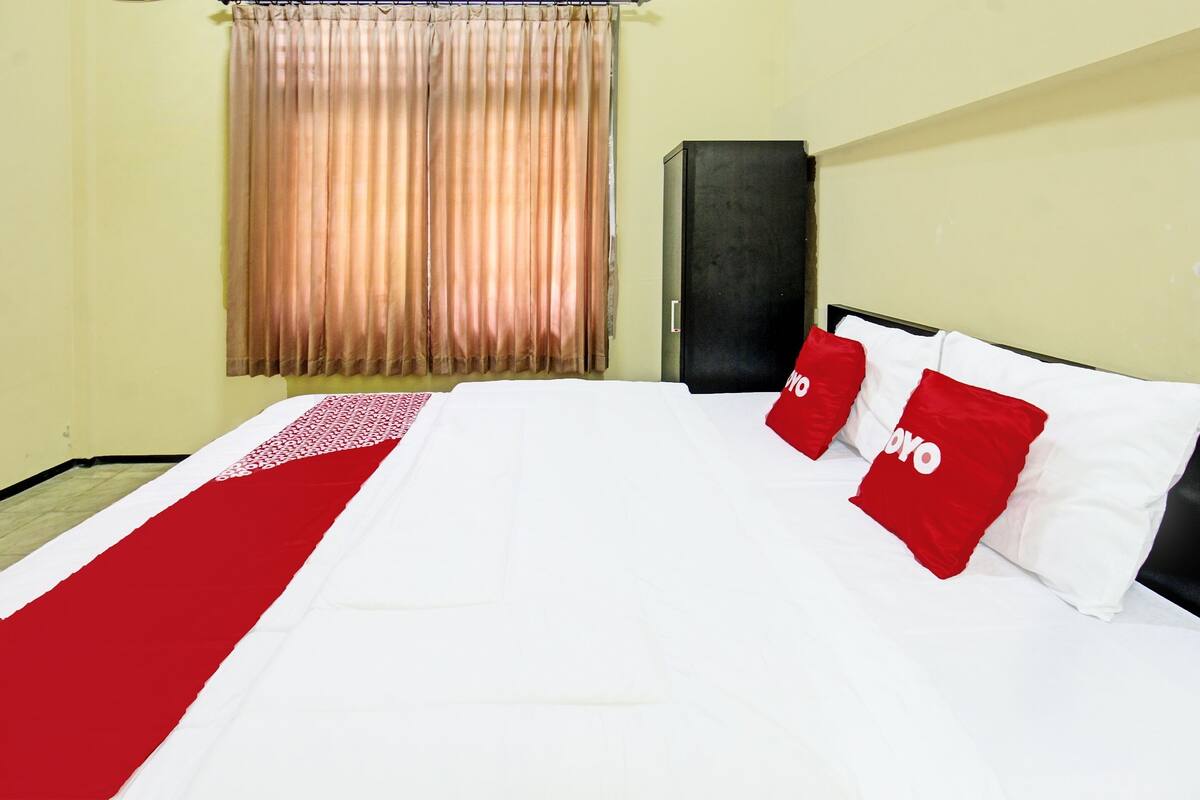 A hotel room with a bed, a wardrobe, and a window with curtains.