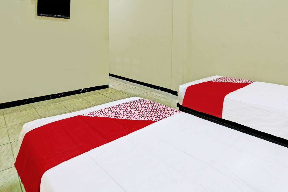 A hotel room with two beds, each with a red and white bedspread, and a small television mounted on the wall.