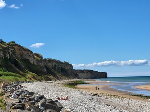 Una spiaggia di ciottoli con scogliere rocciose e cielo azzurro intenso.