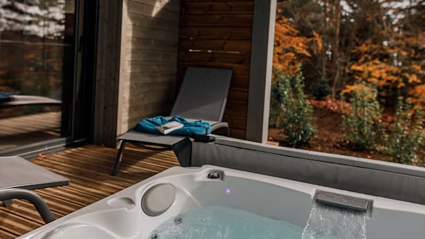 Een hottub met een houten terras en een stoel, omringd door herfstbladeren.