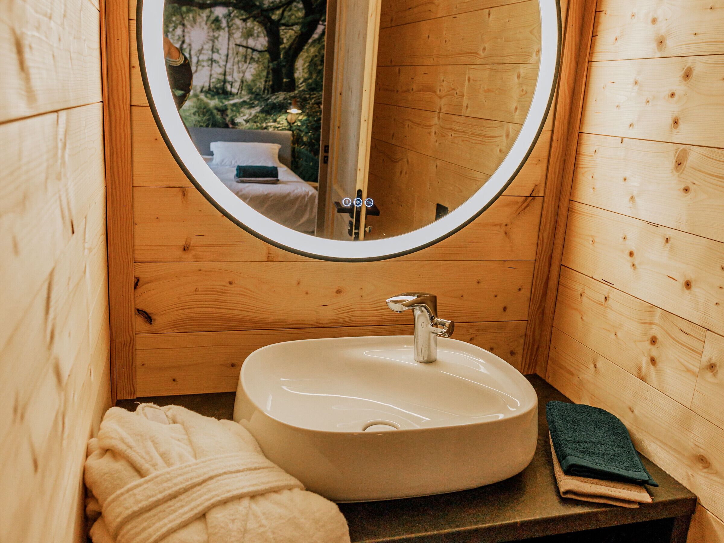 A wooden cabin bathroom with a round mirror, a sink, and a towel.