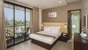 A hotel room with a large bed, a chair, a desk, and a view of the city through large windows. - Hotel DORTN (Paud)