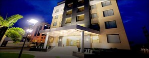 Hotel com vários andares e design moderno, com entrada coberta e diversas varandas.