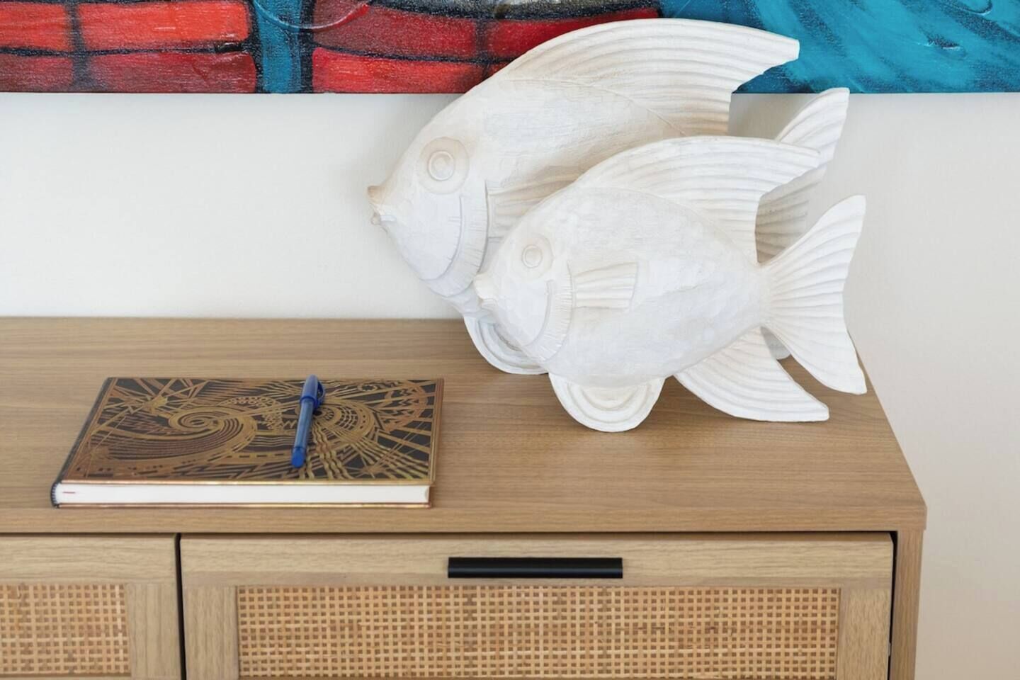 Un meuble en bois orné d’une sculpture de poisson décorative, avec un livre et un stylo.