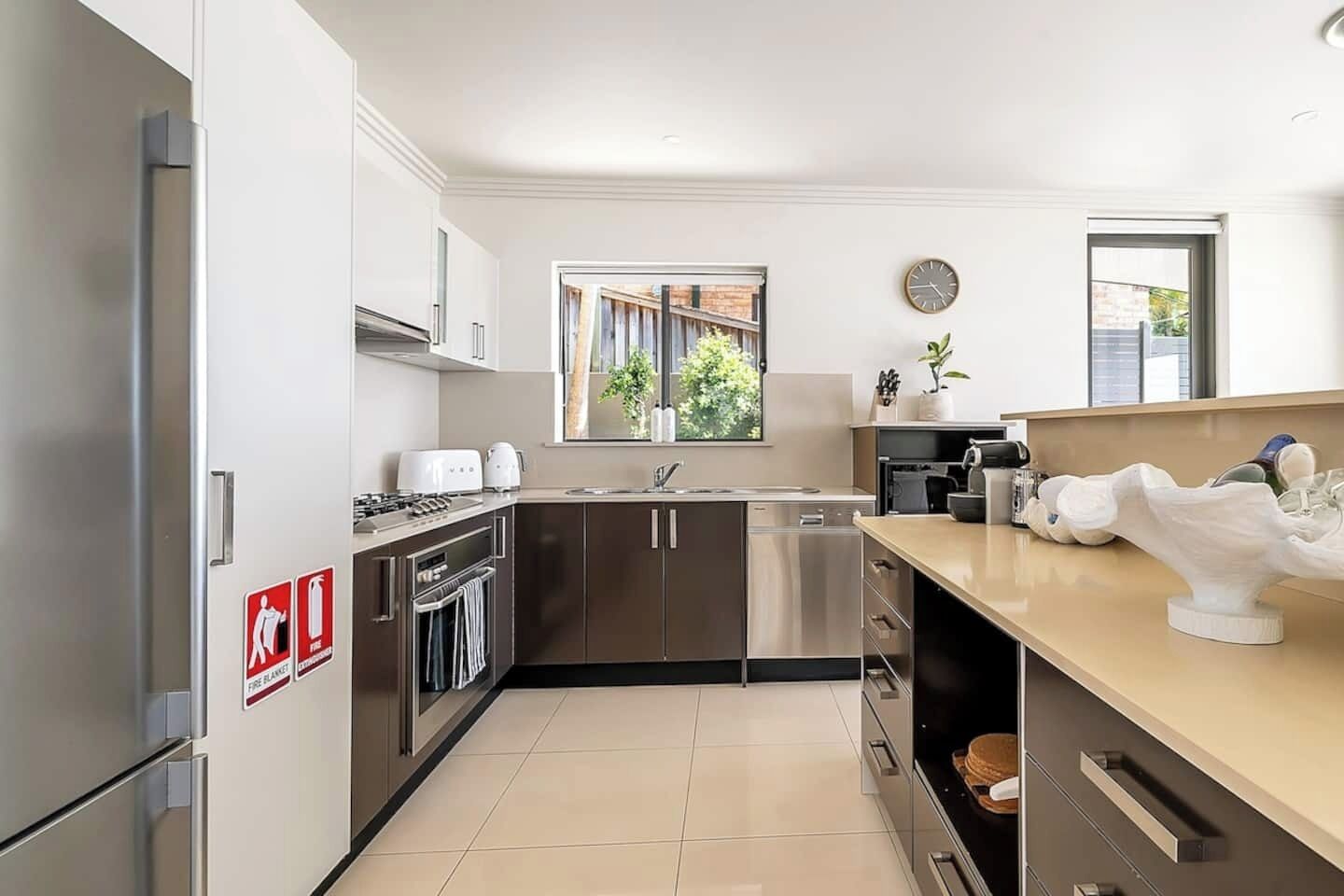 A modern kitchen with stainless steel appliances, a window with a view of greenery, and a fire safety sign.