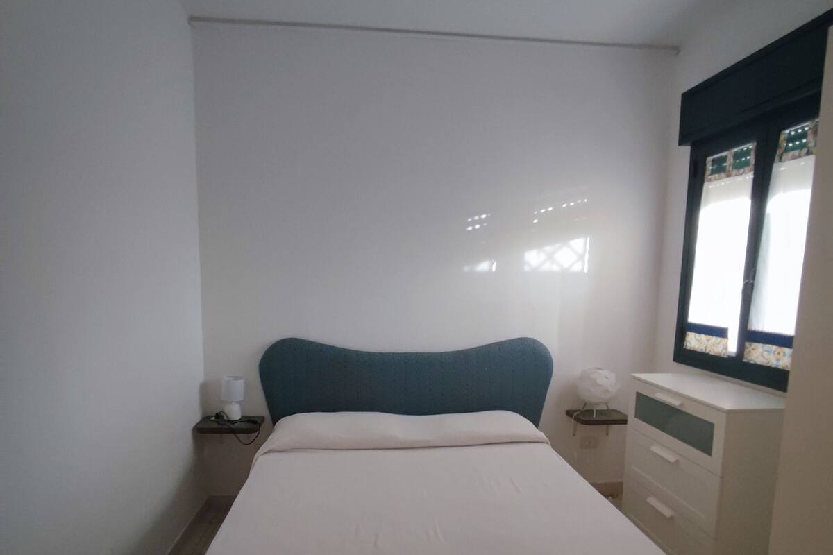 Un dormitorio con cama, mesitas de noche, cómoda y ventana con persianas.