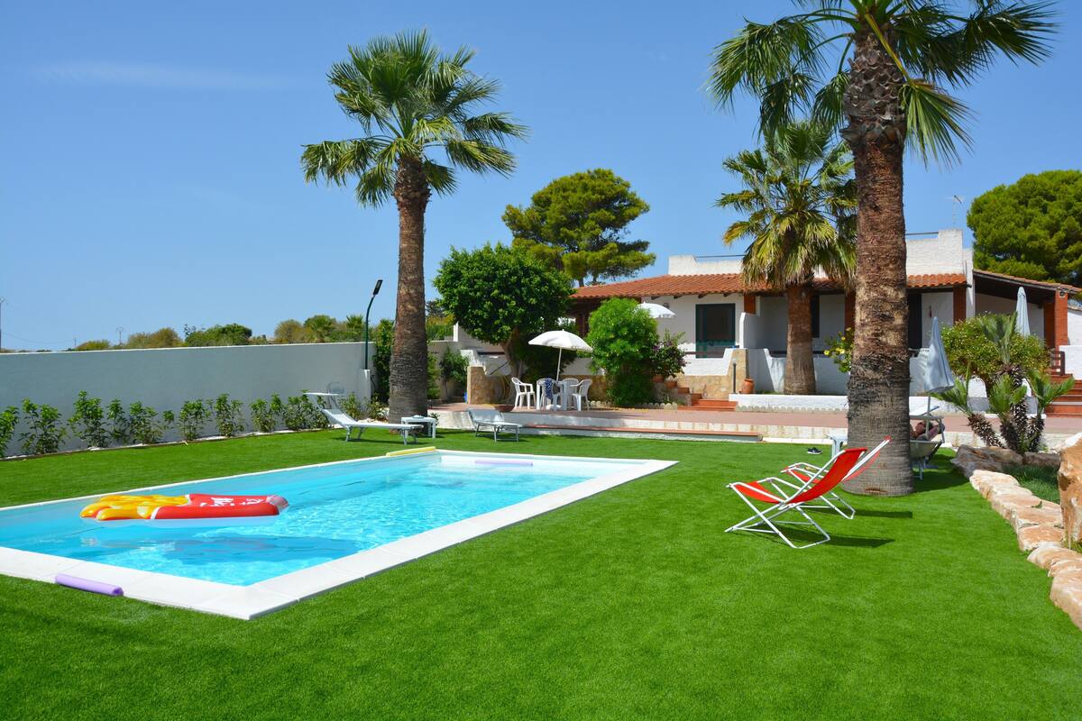 Una piscina con un flotador rojo y amarillo, rodeada de césped verde y palmeras.