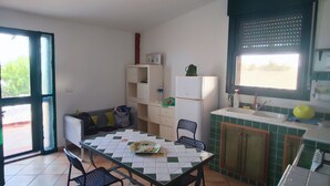 A compact living space with a dining table, chairs, a sofa, a kitchenette, and a window with a view. - Case Tre Palme a San Lorenzo (Noto)