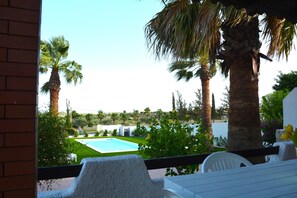 A poolside view with a clear blue sky, palm trees, and a white outdoor seating area.