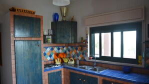 A kitchen with blue cabinets, a tiled backsplash, a window with a view, and a sink. - Case Tre Palme a San Lorenzo (Noto)