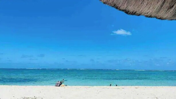 A beach with clear blue water and a thatched umbrella.