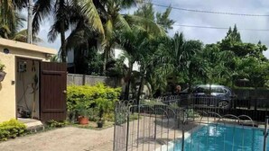 A swimming pool with a metal fence, surrounded by palm trees and a wooden fence.