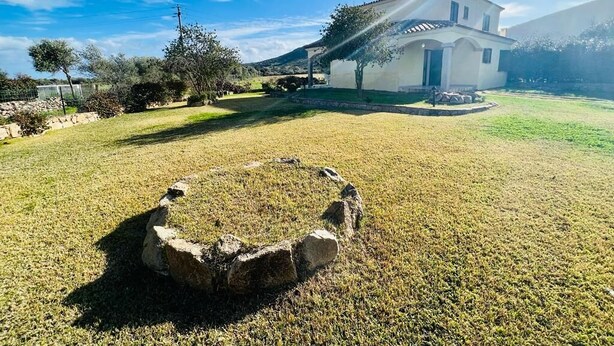 A white house with a stone fire pit in the front yard. - Casa Vacanza L'alzoni (San Teodoro)