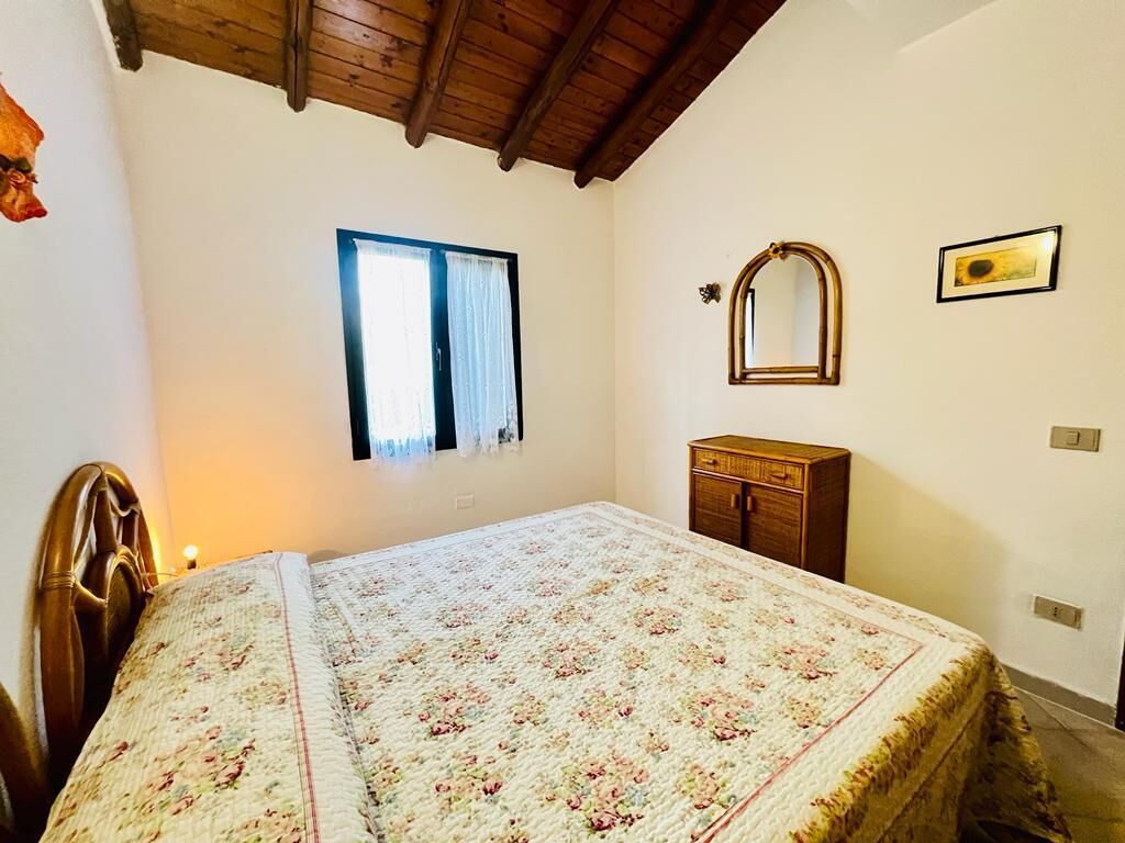 A bedroom with a bed, a window, a wooden cabinet, and a mirror on the wall.