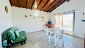 A room with a wooden ceiling, a green sofa, a dining table with chairs, and a small cabinet. - Casa Vacanza L'alzoni (San Teodoro)