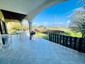 Eine überdachte Terrasse mit Fliesenboden, weißen Stühlen und einem kleinen Tisch.