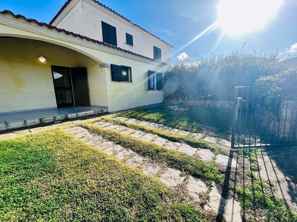 Une maison avec une terrasse dallée, un chemin en pierre et un portail en métal.