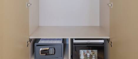 A walk-in closet with a hanging rod, a small safe, and a mini refrigerator.