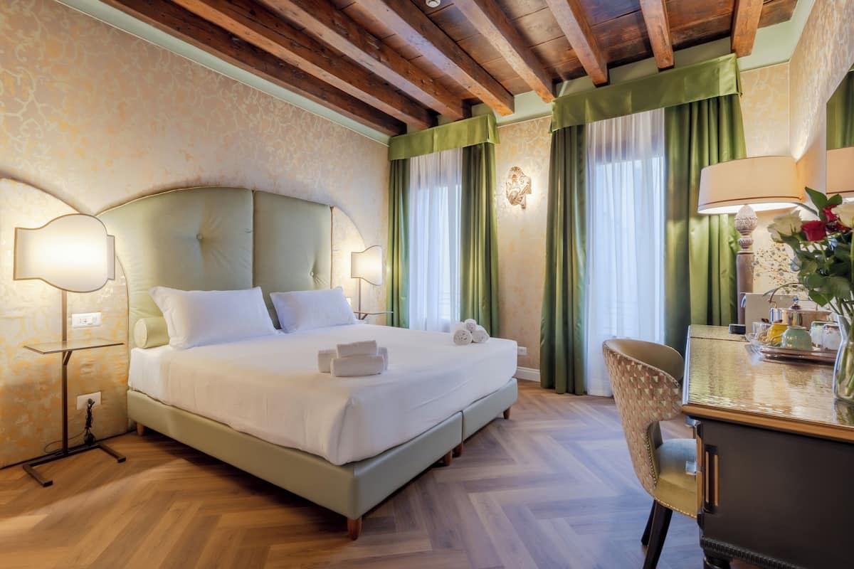 A hotel room with a large bed, a desk with a lamp, and a chair.