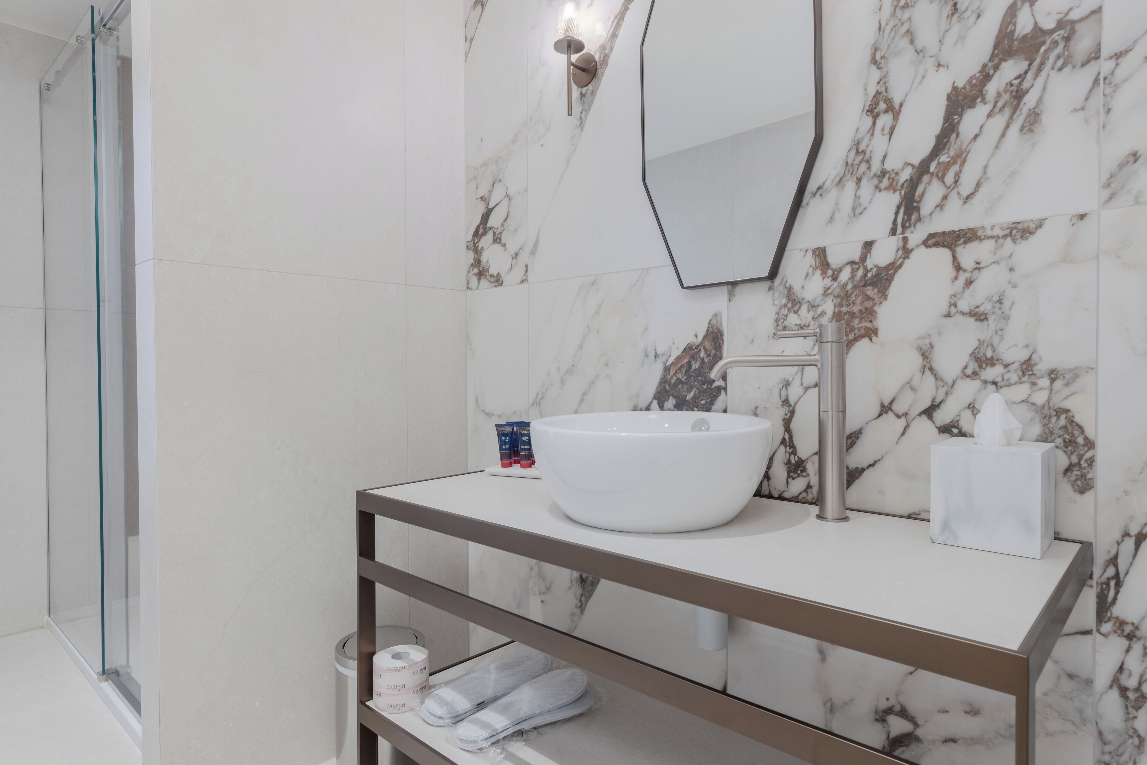 A modern bathroom with a white sink, a mirror, and a marble backsplash.