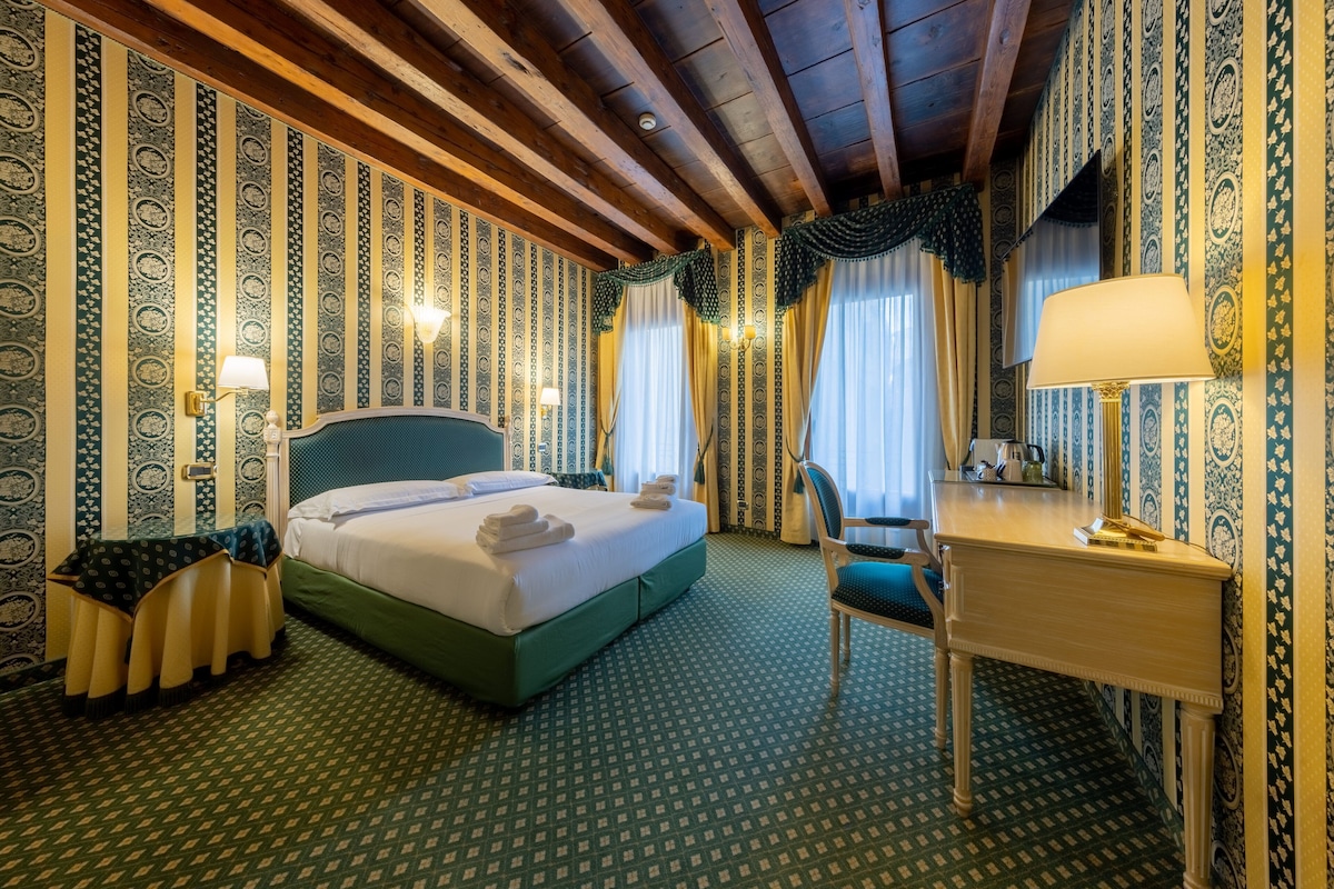 A hotel room with a bed, desk, chair, and patterned wallpaper.