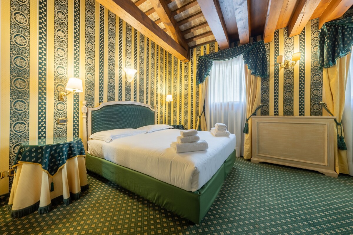 A hotel room with a bed, a table with chairs, a radiator, and patterned wallpaper.