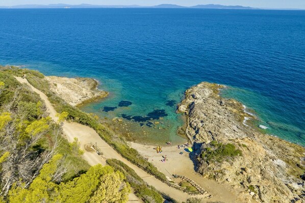 Un paysage côtier caractérisé par une eau d’un bleu limpide, un terrain rocheux et un sentier de terre menant à une plage.