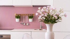 A modern kitchen with white cabinets, a pink backsplash, and a white vase with pink flowers on the counter. - Venetian Palace Gold Apartment with Balcony R&R (Venecia)