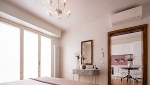 A bedroom with a large bed, a bedside table with a mirror, and a view of the kitchen through an open door. - Venetian Palace Gold Apartment with Balcony R&R (Venecia)