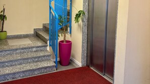A hotel lobby with a red carpet, a blue staircase, a large potted plant, and an elevator. - BLU HOTEL 4 4 S.R.L. (Buccinasco)