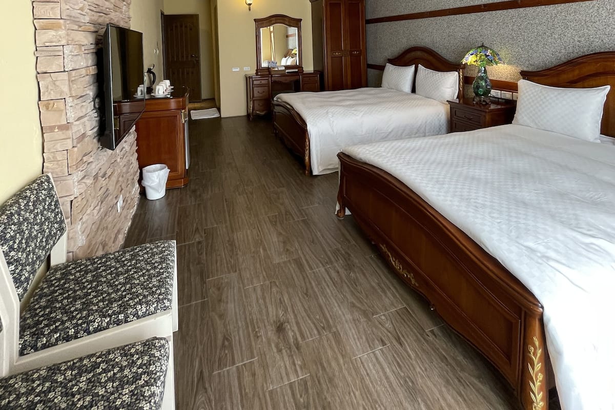 A hotel room with two beds, a stone accent wall, wooden beams, a flat-screen TV, and a stone fireplace.