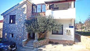 Una casa de dos pisos con fachada de piedra, un balcón y un pequeño árbol en el frente.
