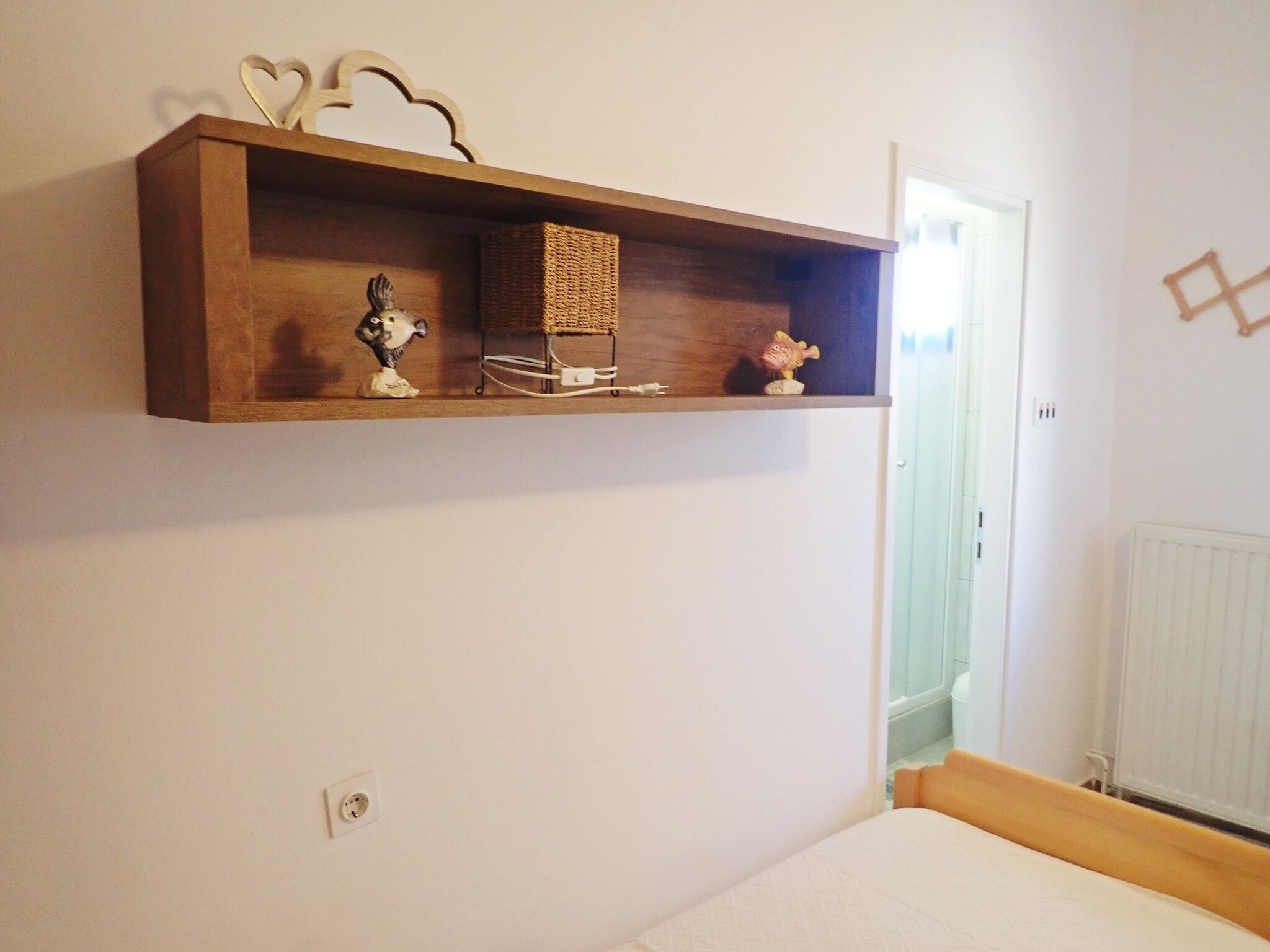 Een slaapkamer met een houten plank boven het bed, waarop decoratieve objecten en een mand staan.