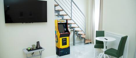 Un salon moderne doté d’un téléviseur à écran plat, d’une borne d’arcade rétro, d’une petite table avec une télécommande et d’un escalier.