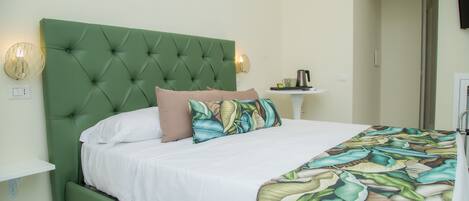 A neatly made bed with a green upholstered headboard, white bedding, and a tropical leaf-patterned throw.