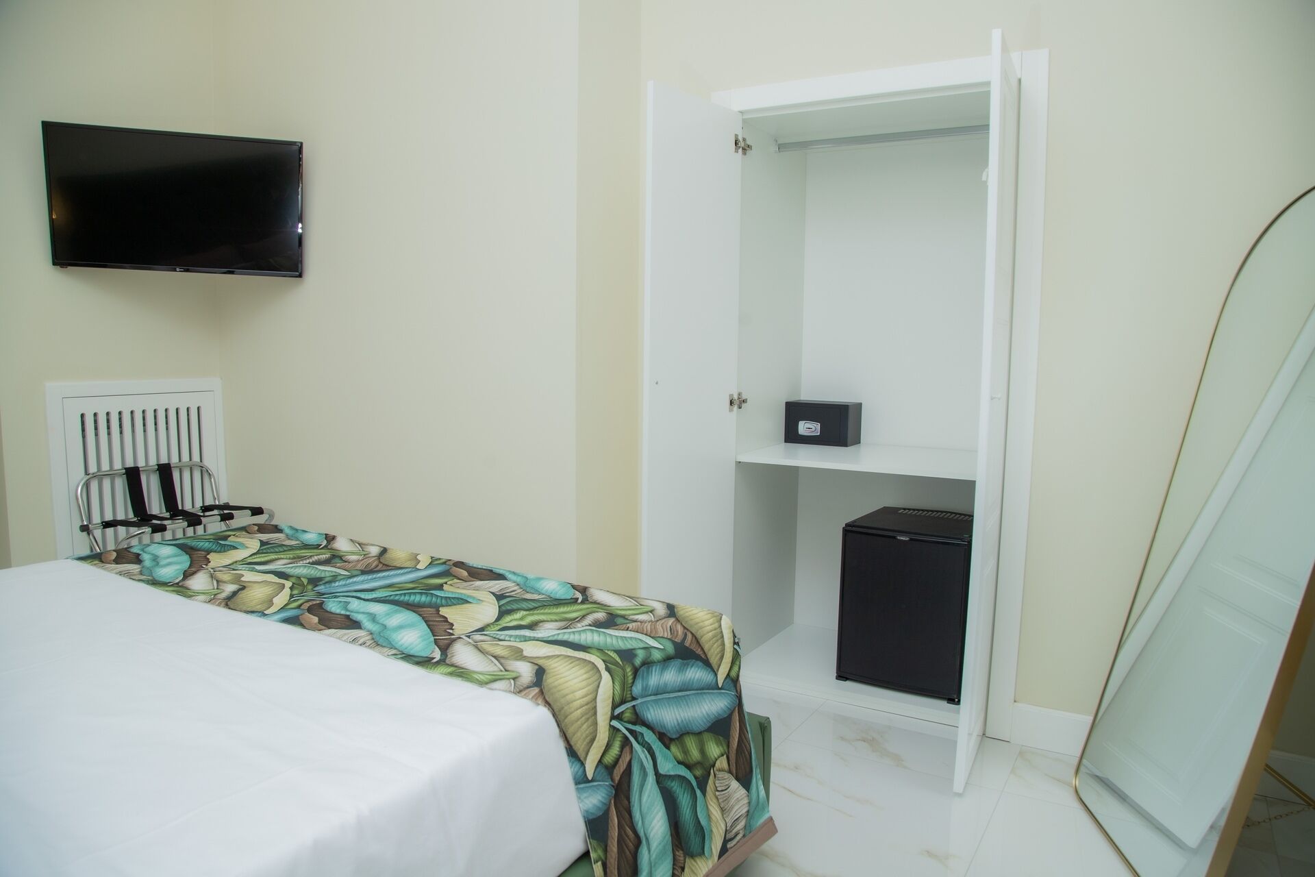 Ein Schlafzimmer mit einem Bett, einem an der Wand montierten Fernseher, einem Kleiderschrank und einem kleinen Schreibtisch mit einem Computer.