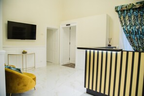Una sala de estar moderna con televisor de pantalla plana, un sofá amarillo, piso de mármol blanco y un mostrador de recepción.