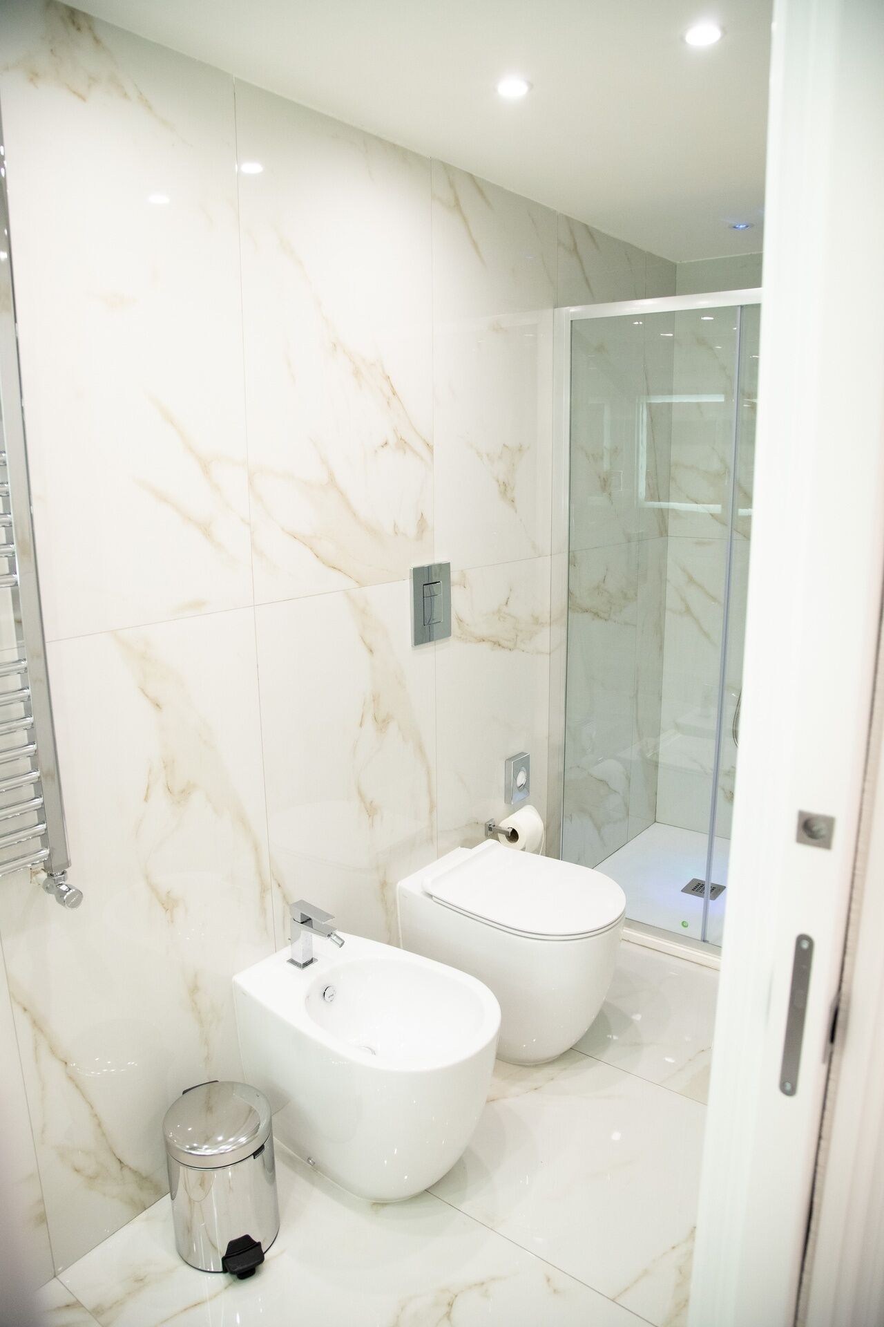 A modern bathroom with two bidets, a glass shower enclosure, and a toilet.